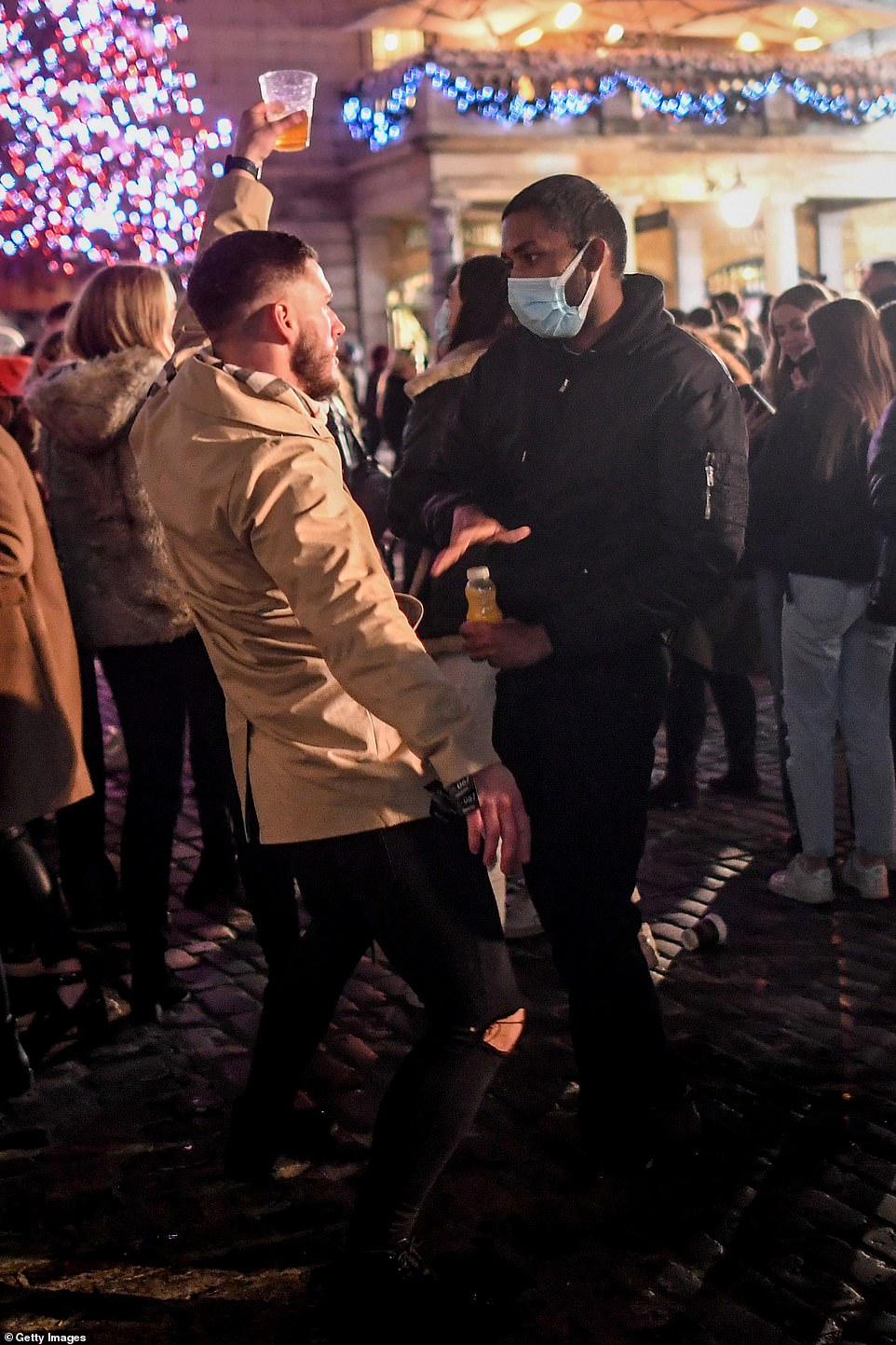 A man carrying a pint dances in front of a man wearing a mask in Covent Garden in London's West End on December 5